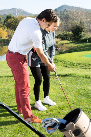 Positive man golf trainer showing woman player how to hit ball rightlyの写真素材