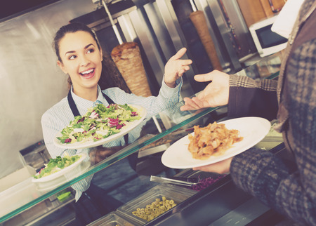 Positive female worker serving customer with smile at shawarma placeの写真素材
