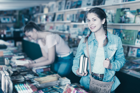 Portrait of smiling teenage girl selecting book in book storeの写真素材