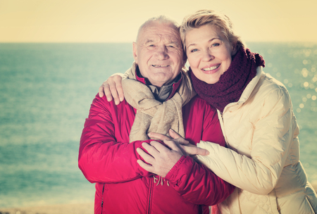 Aged husband and wife taking stroll on beach in cold seasonの写真素材