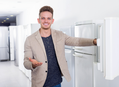 Happy young man selecting domestic refrigerator in supermarketの写真素材