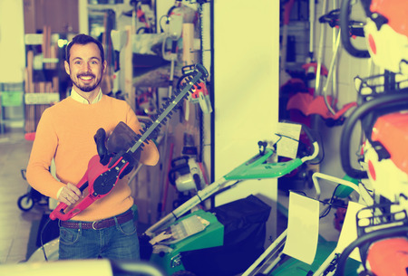 Young happy cheerful  man choosing hedge cutter in garden equipment shopの写真素材