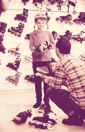 Smiling american male seller putting roller-skates on boy customer in sports storeの写真素材