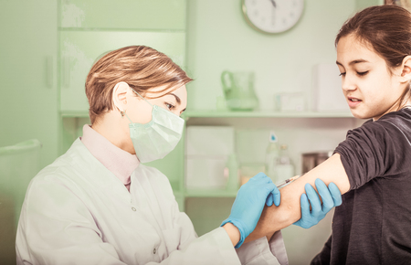 Nurse in medical mask does compulsory vaccination to girl in hospitalの写真素材