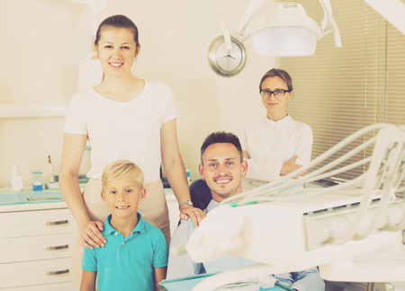 Father of the family is sitting in dental chair near his wife with child in clinic.の写真素材