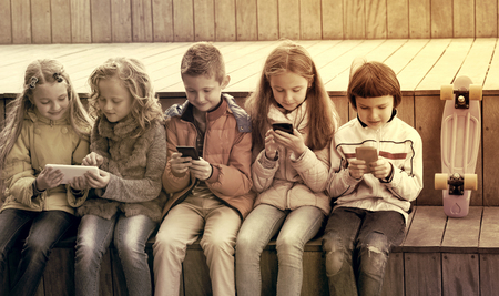 Outdoor portrait of cheerful girls and boys playing with phonesの写真素材