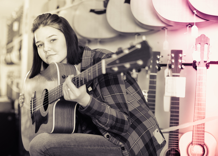 Teenage girl choosing best acoustic guitar in a guitar shopの写真素材