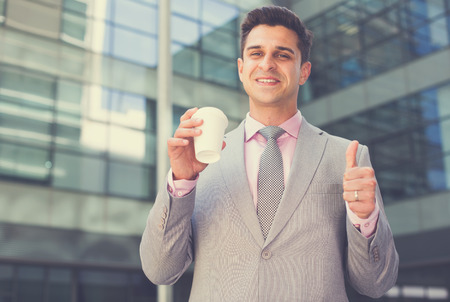 Smiling businessman with cup of coffee showing thumb as sign of successの写真素材