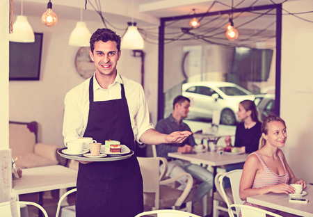 Positive smiling waiter holding served tray meeting visitors at pastry barの写真素材