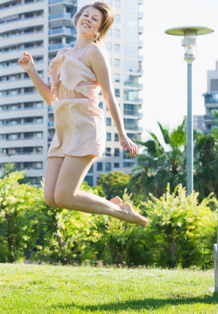 Young girl is playfully jumping in the park in lighty dress.の写真素材
