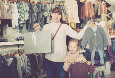 Happy pregnant woman and girl enjoying purchases in childrens cloths shopの写真素材