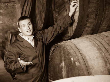 Smiling man in robe checking ageing barrel process of wineの写真素材