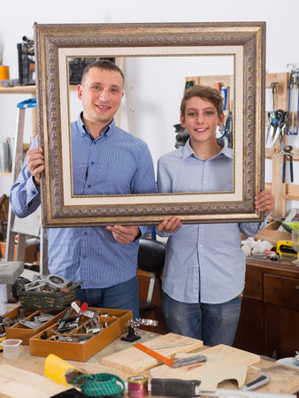portrait of  happy american  man and boy choosing tight wooden bar in picture framing atelier
