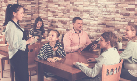 Father, mother and children are giving order to cheerful waitress in comfy cafe.の写真素材