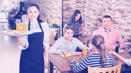 happy young waitress warmly welcoming guests to comfortable family cafeの写真素材