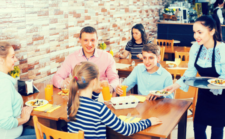 Woman is bringing salad and juice to young visitors of family cafe.の写真素材