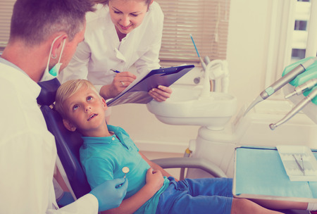 Dentist with woman assistant are diagnosticating to young patient which is sitting in dental clinic.の写真素材