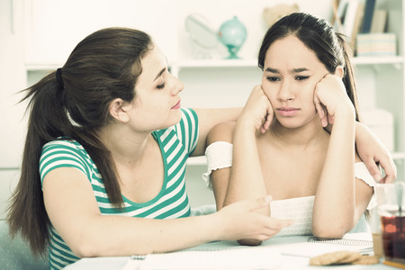 Teens girl comforting her upset female friend at home tableの写真素材