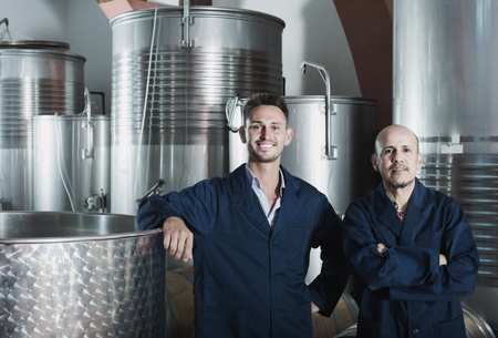 Two adult winery employees wearing coats standing in fermentation section on winery manufactoryの写真素材