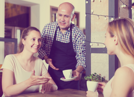 Two young happy english girls meeting in cafe and drinking tasty coffeeの写真素材