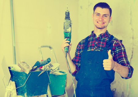 Male worker is standing with drill in hands in repairable room.の写真素材