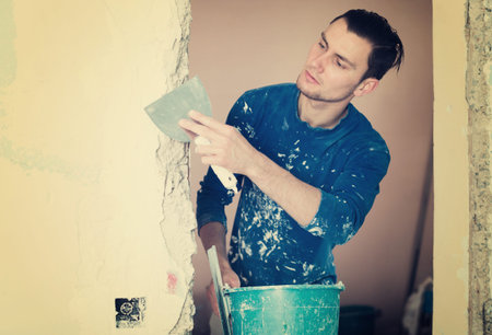 Construction worker wearing casual clothing with wall plastering tools renovating apartment houseの写真素材