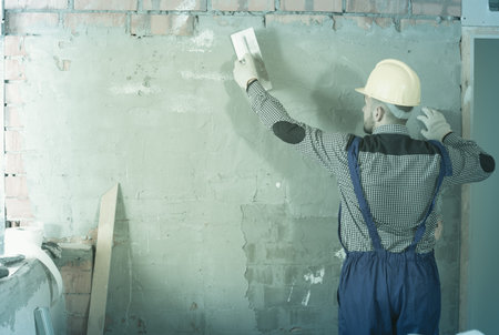 Man in the helmet is plastering the wall at the house.