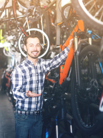 Young smiling man looks at bicycle frame in sports shopの写真素材