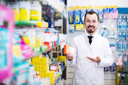 Glad male pharmacist offering reliable medicine preparations in drugstoreの写真素材