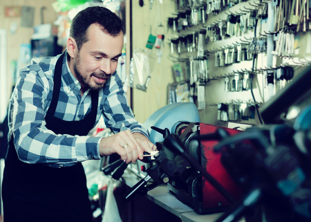 Smiling male worker shaping new key in repair workshopの写真素材
