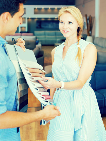 Smiling young woman is consulting with the seller about the choice of a colors of sofaの写真素材