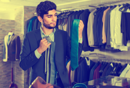 Smiling male is picking up tie for suit in men's shop.の写真素材
