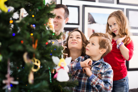 Cheerful family putting decorations on Christmas tree at homeの写真素材