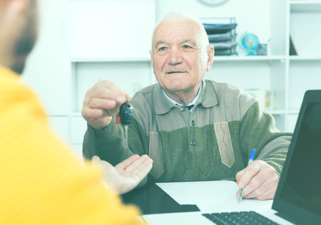 Elderly man and young manager sign car purchase contract and hand over keysの写真素材