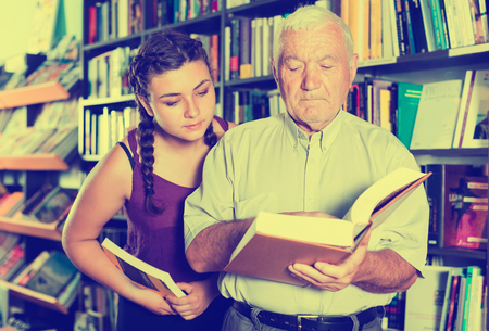 Senior man with young woman are reading books in bookstore.の写真素材