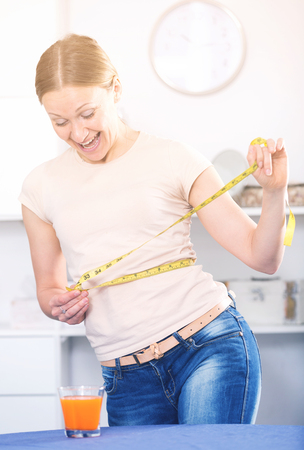 Smiling young woman measuring waist with yellow tapeの写真素材