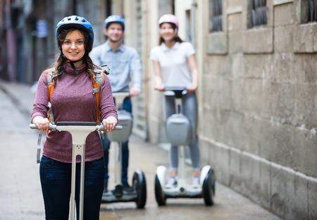 Company of joyful  smiling friends riding on segways by city streetsの写真素材