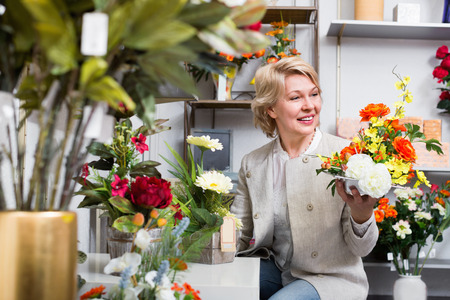 Happy positive  mature blond woman selecting flowers in storeの写真素材