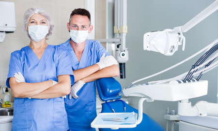 Two professional confident dentists posing near a dental chair in clinic. Focus on both personsの写真素材