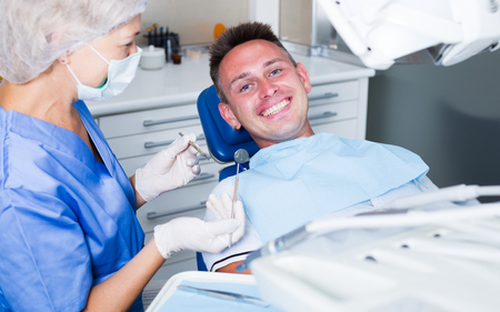 Male patient sitting on chair in dental office getting dentist treatmentの写真素材