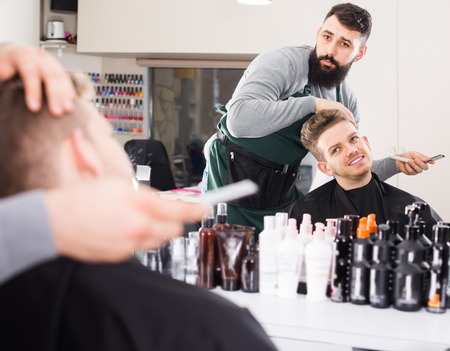 Smiling man hairdresser making haircut to client at hair salonの写真素材
