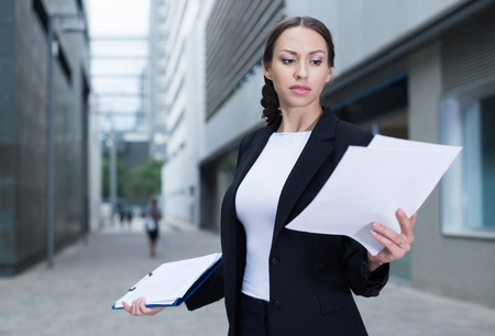 Serious female employee is dissatisfied of the results of the financial report outdoors.の写真素材