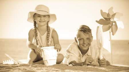 happy two kids in elementary school playing with toys on beach on summer dayの写真素材