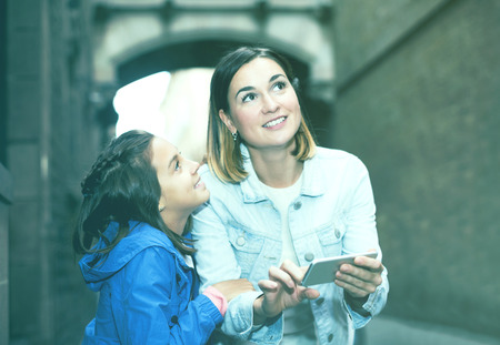 Young mother and daughter consulting guide in phone during sightseeing tourの写真素材