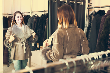 Positive girl customer deciding on the choice of sheepskin coat in womens cloths storeの写真素材