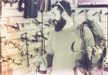 concentrated male customer examining assortment of climbing equipment in sports equipment storeの写真素材