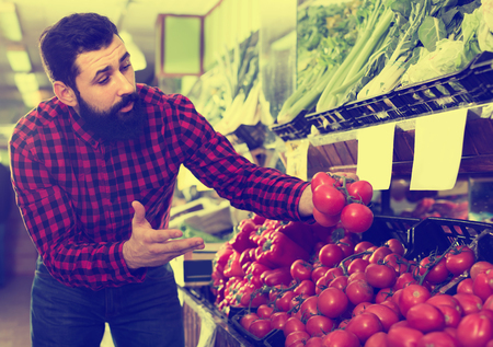Smiling male seller showing fresh tomatoes in grocery shop indoorsの写真素材