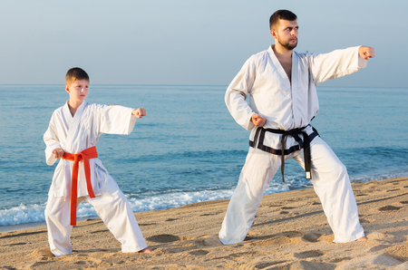 Positive adult man and boy exercising karate in morning outdoorの写真素材