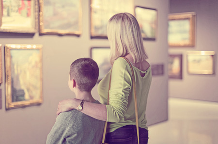 happy european mother and son looking at paintings in halls of museumの写真素材