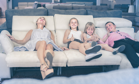 Cheerful family with children are choosing new sofa-transformer in furniture store.の写真素材